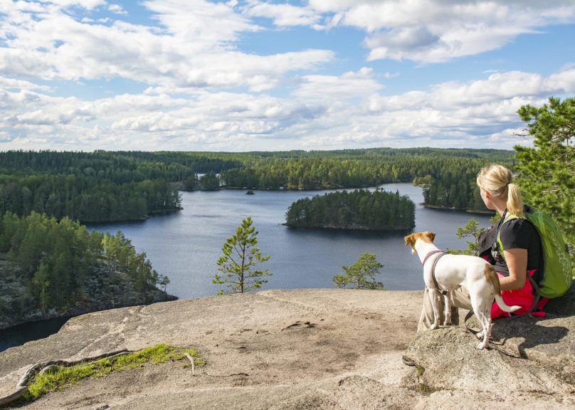 Nainen istuu kalliolla koiransa kanssa.