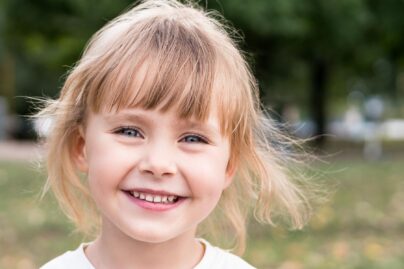Ruskeatukkainen pieni tyttö katsoo suoraan kameraan ja hymyilee iloisesti.