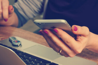 Nainen tietokoneella kännykkä kädessä