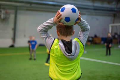 Puolikuvassa selin oleva poika heittää jalkapalloa