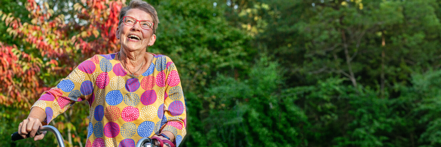 Iäkäs nainen taluttaa pyörää ja hymyilee