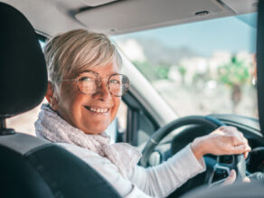 Seniorinainen auton ratissa katsoo hymyillen kameraan