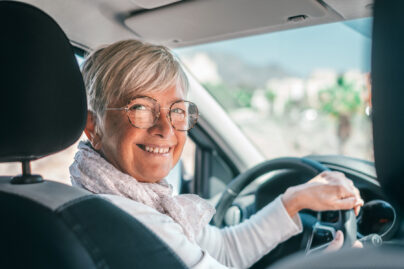 Seniorinainen auton ratissa katsoo hymyillen kameraan