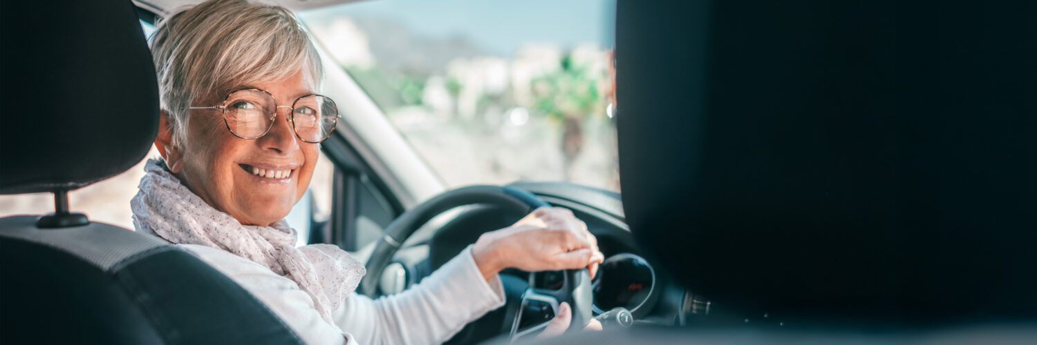 Seniorinainen katsoo hymyillen kameraan autossa