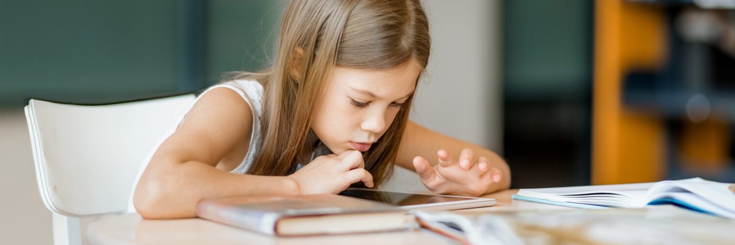 Alakouluikäinen tyttö apeana selaa tablettia