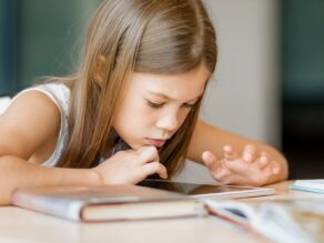 Alakouluikäinen tyttö apeana selaa tablettia