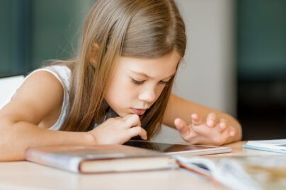 Alakouluikäinen tyttö apeana selaa tablettia