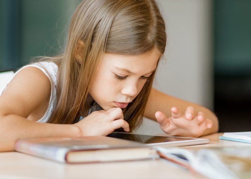 Alakouluikäinen tyttö apeana selaa tablettia