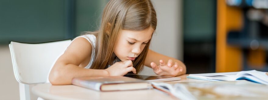 Alakouluikäinen tyttö apeana selaa tablettia