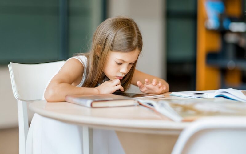 Alakouluikäinen tyttö apeana selaa tablettia