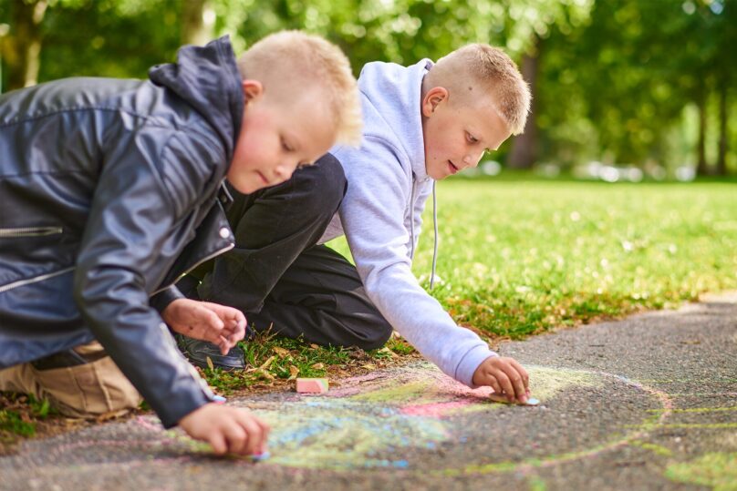 Kouluikäiset pojat piirtävät katuliidulla maahan puistossa