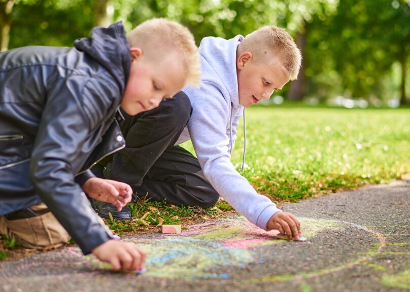 Kouluikäiset pojat piirtävät katuliidulla maahan puistossa