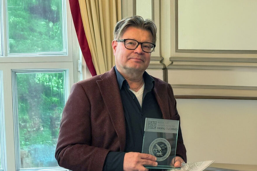 Puolikuvassa patologi Hannu Tuominen, joka on voittanut vuoden 2025 patologi -palkinnon. Hannu pitää Suomen IAP:n myöntämää palkintoa kädessään.