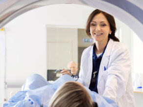 Puolikuvassa hymyilevä naislääkäri ja potilas menossa kuvantamistutkimukseen