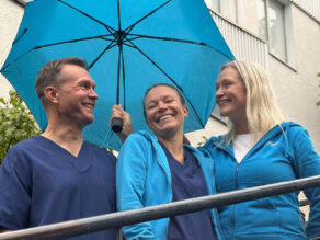 Sateenvarjon alla hymyilevat tähystysklinikan kolme työntekijää.