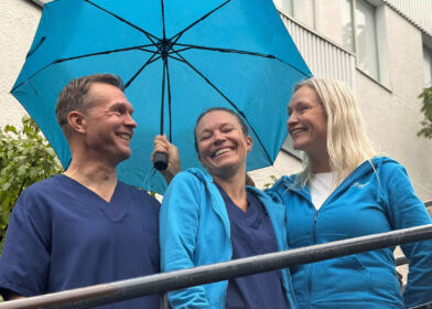 Sateenvarjon alla hymyilevat tähystysklinikan kolme työntekijää.