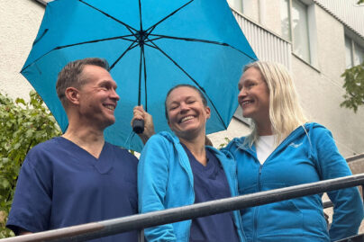 Sateenvarjon alla hymyilevat tähystysklinikan kolme työntekijää.