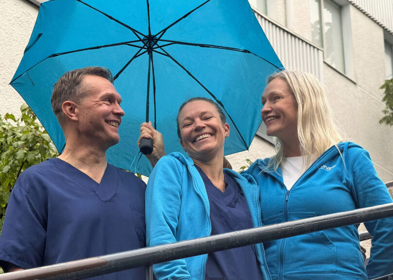 Sateenvarjon alla hymyilevat tähystysklinikan kolme työntekijää.