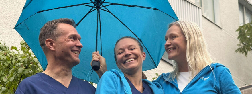 Sateenvarjon alla hymyilevät kolme Tilkan tähystysklinikan työntekijää.