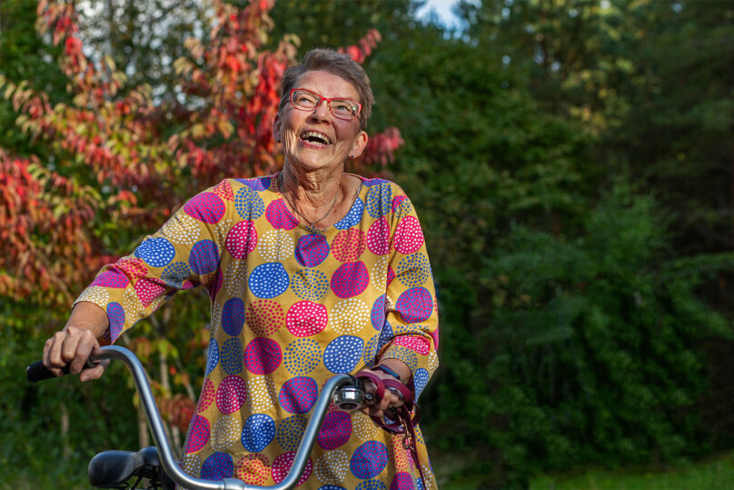 Seniorinainen taluttaa pyörää ja hymyilee
