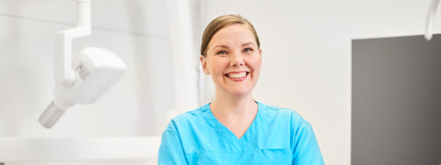 Hammasklinikan työntekijänainen hymyilee puolikuvassa