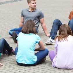 Kuntoutuskurssin tai -valmennuksen nuoret istuvat ulkona ympyrässä keskustelemassa.