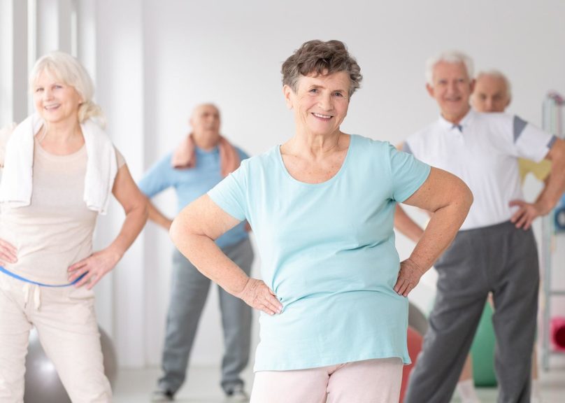 seniorinaiset ja miehet jumppaavat hymyillen sisalla