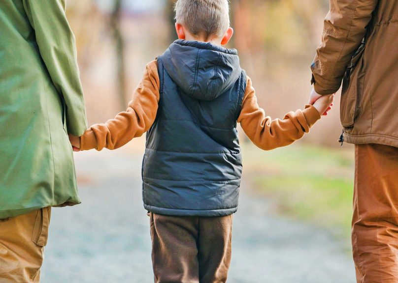 poikalapsi kavelee tiella ja pitaa kiinni vanhempien kasista