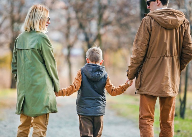 poikalapsi kavelee tiella ja pitaa kiinni vanhempien kasista