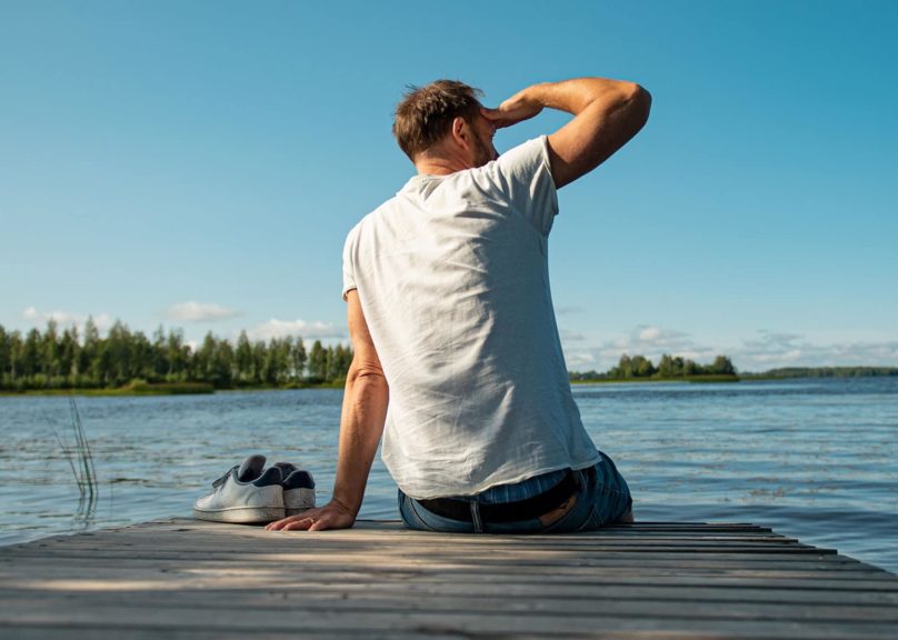 mies istuu laiturin reunalla kasi otsalla