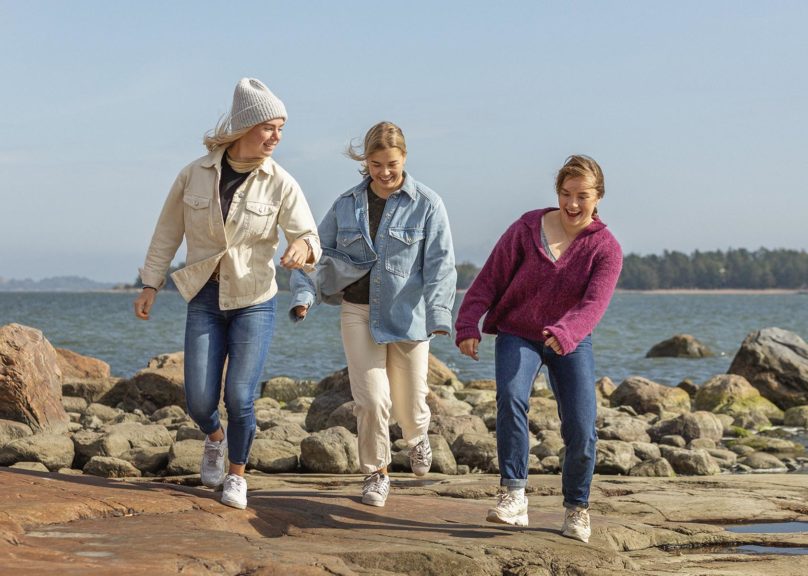 Kolme nuorta ystävystä kävelee iloisina rannalla