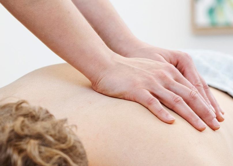 Fysioterapeutti hieroo miesasiakkaan selkää.