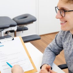 Coronarian fysioterapeutti ja miesasiakas hymyilevät toisilleen fysioterapian alkukartoituskeskustelussa pöydän ääressä.