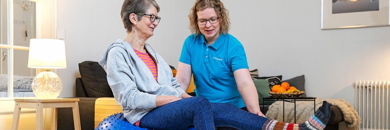 Coronarian seniorifysioterapian fysioterapeutti ohjaa seniorinaisasiakasta fysioterapialiikkeessä kotiympäristössä.
