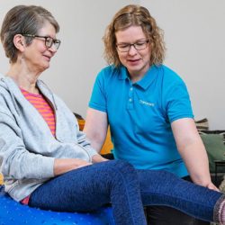 Coronarian seniorifysioterapian fysioterapeutti ohjaa seniorinaisasiakasta fysioterapialiikkeessä kotiympäristössä.