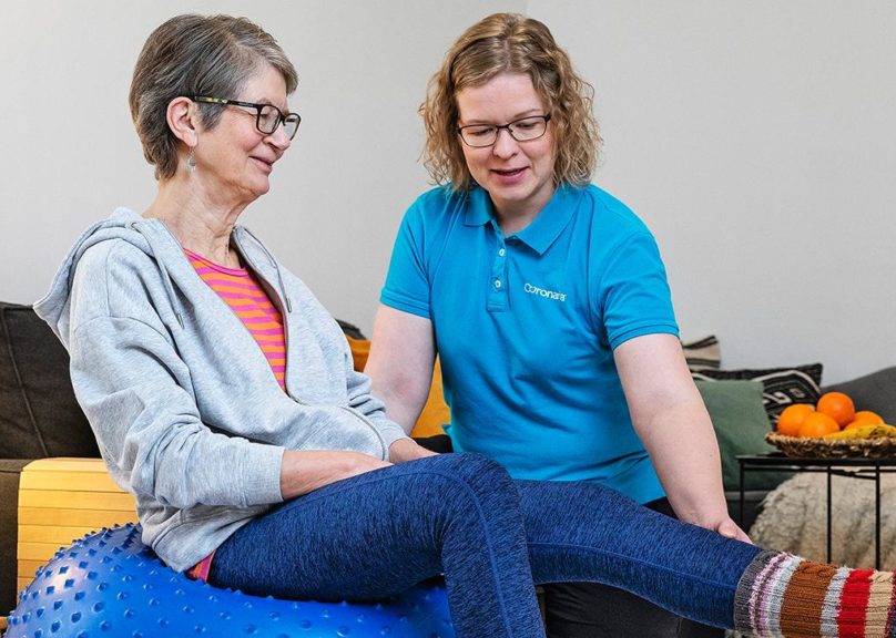 Coronarian seniorifysioterapian fysioterapeutti ohjaa seniorinaisasiakasta fysioterapialiikkeessä kotiympäristössä.