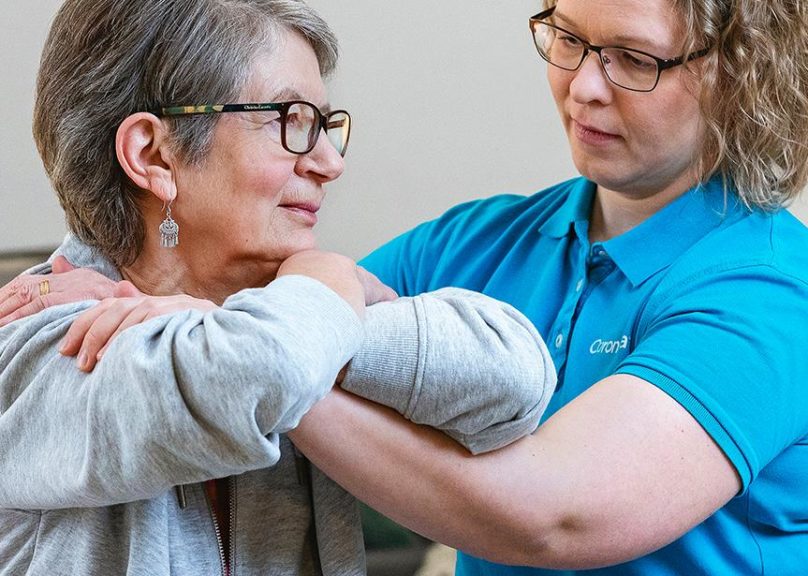 Seniorinaisasiakas ja fysioterapeutti keskittyvät fysioterapialiikkeeseen asiakkaan kotona.