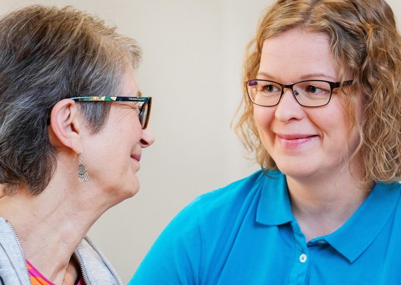 Seniorinainen ja naisfysioterapeutti katsovat toisiinsa ja hymyilevät.
