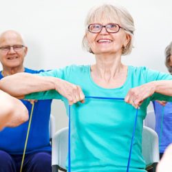 Seniorinaiset ja seniorimiehet jumppaavat kuminauhalla.