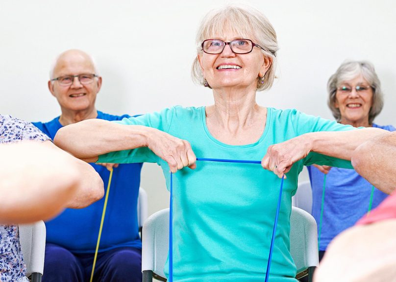 Seniorinaiset ja seniorimiehet jumppaavat kuminauhalla.