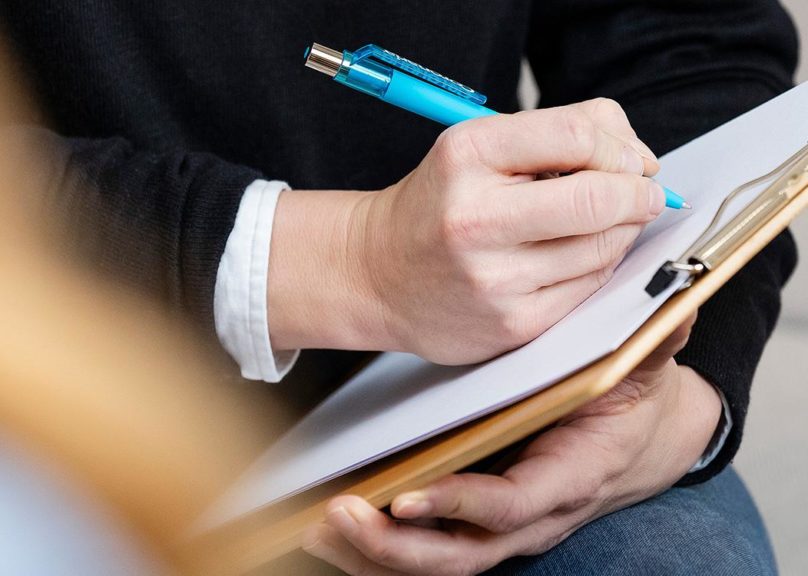 Lähikuva psykologin käsistä, kun hän kirjaa asioita paperille.