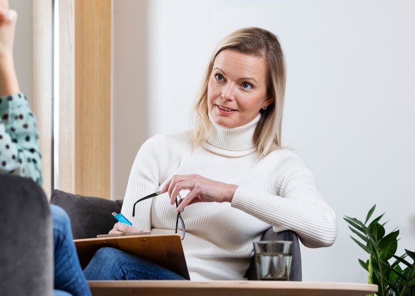 terapeutti nainen istuu tuolilla ja katsoo asiakkaan suuntaan