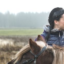 Peltomaisemaa vasten tummahiuksinen nainen ja tyttö, joka on hevosen selässä.