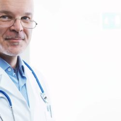 Iäkäs mieslääkäri katsoo kohti stetoskooppi kaulassa.