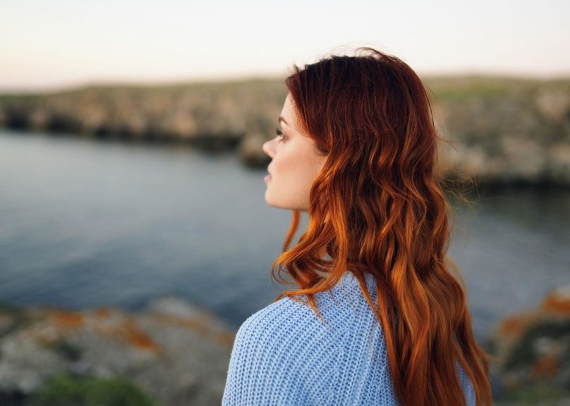 nuori punahiuksinen nainen katsoo horisonttiin ulkona veden aarella