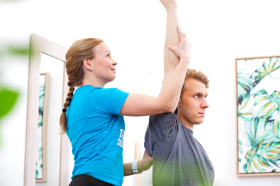 Naisterapeutti auttaa miesasiakasta käden nostossa suoraan ylöspäin