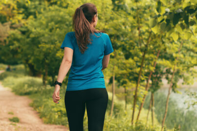 nainen kävelee kesäistä metsäpolkua vesistön lähellä