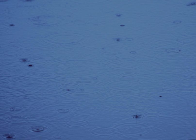 Tummansininen vedenpinta, jossa sadepisaroiden synnyttämiä renkaita.