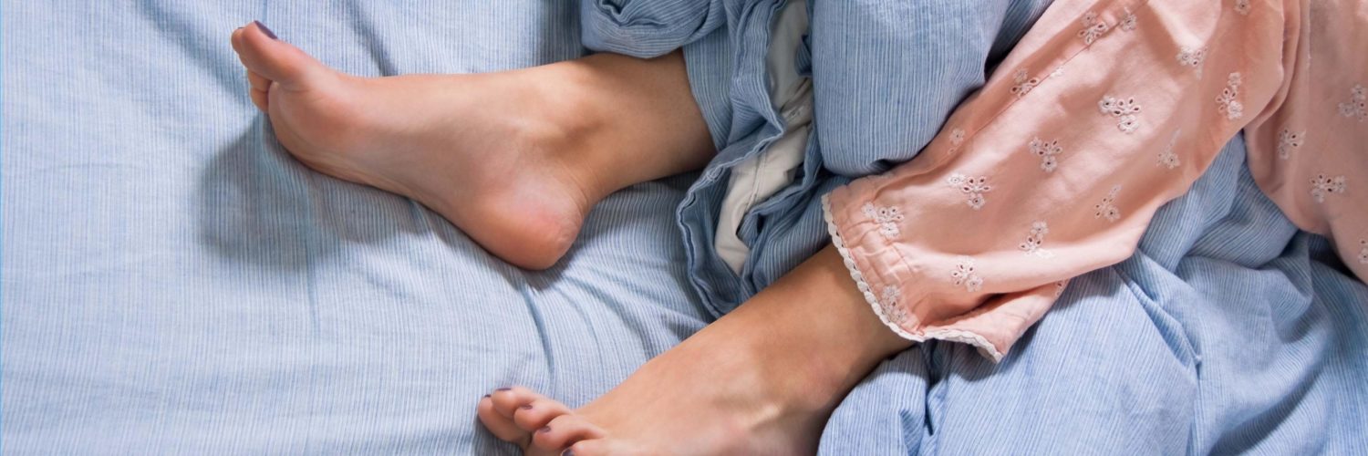 Nukkuvan naisen jalat sängyllä, osittain peiton seassa