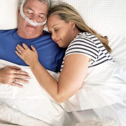 Varttunut pariskunta nukkumassa sängyssä ja miehellä on CPAP-laite.
